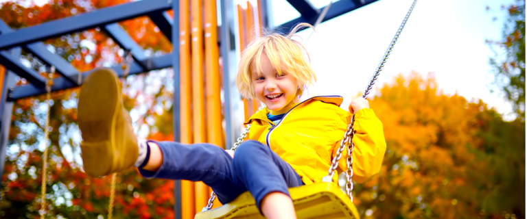 Child in yellow jacket with blonde hair on swings with bright colors