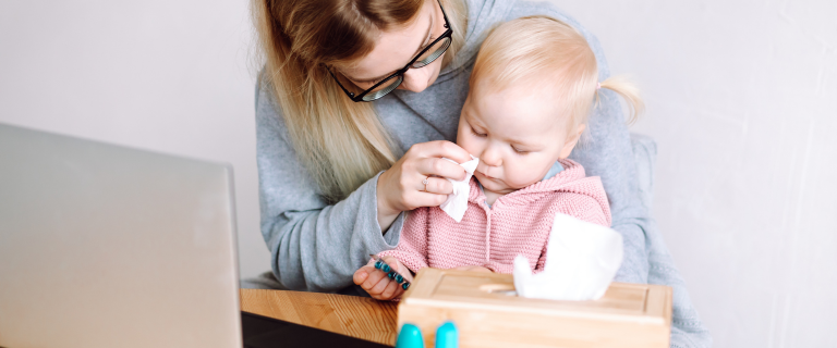 Woman holding baby with blonde hair in pink outfit looking at computer