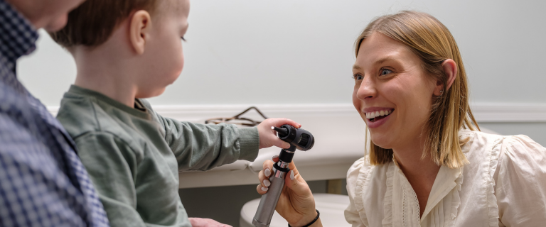 Female doctor smiling at young boy being held by man/father