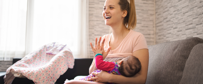 Woman in pink holding and feeding baby while sitting on couch